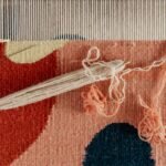 From above of shuttle and needle placed on part of handmade carpet with circle pattern on loom frame during weaving process
