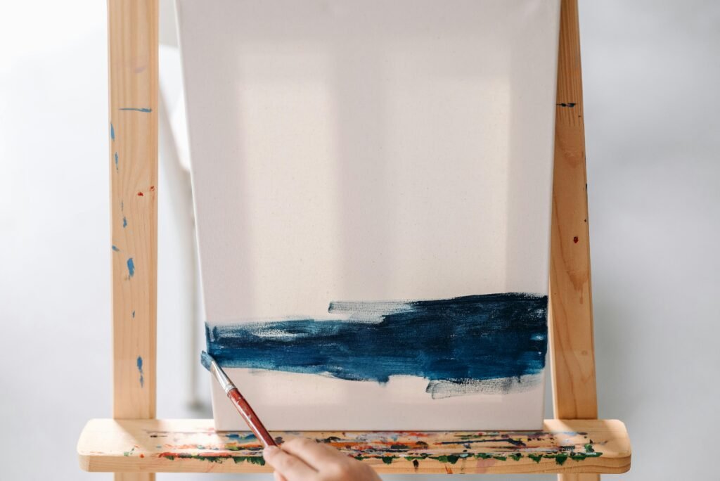 Close-up of an artist painting a blue stroke on canvas using a paintbrush on an easel.